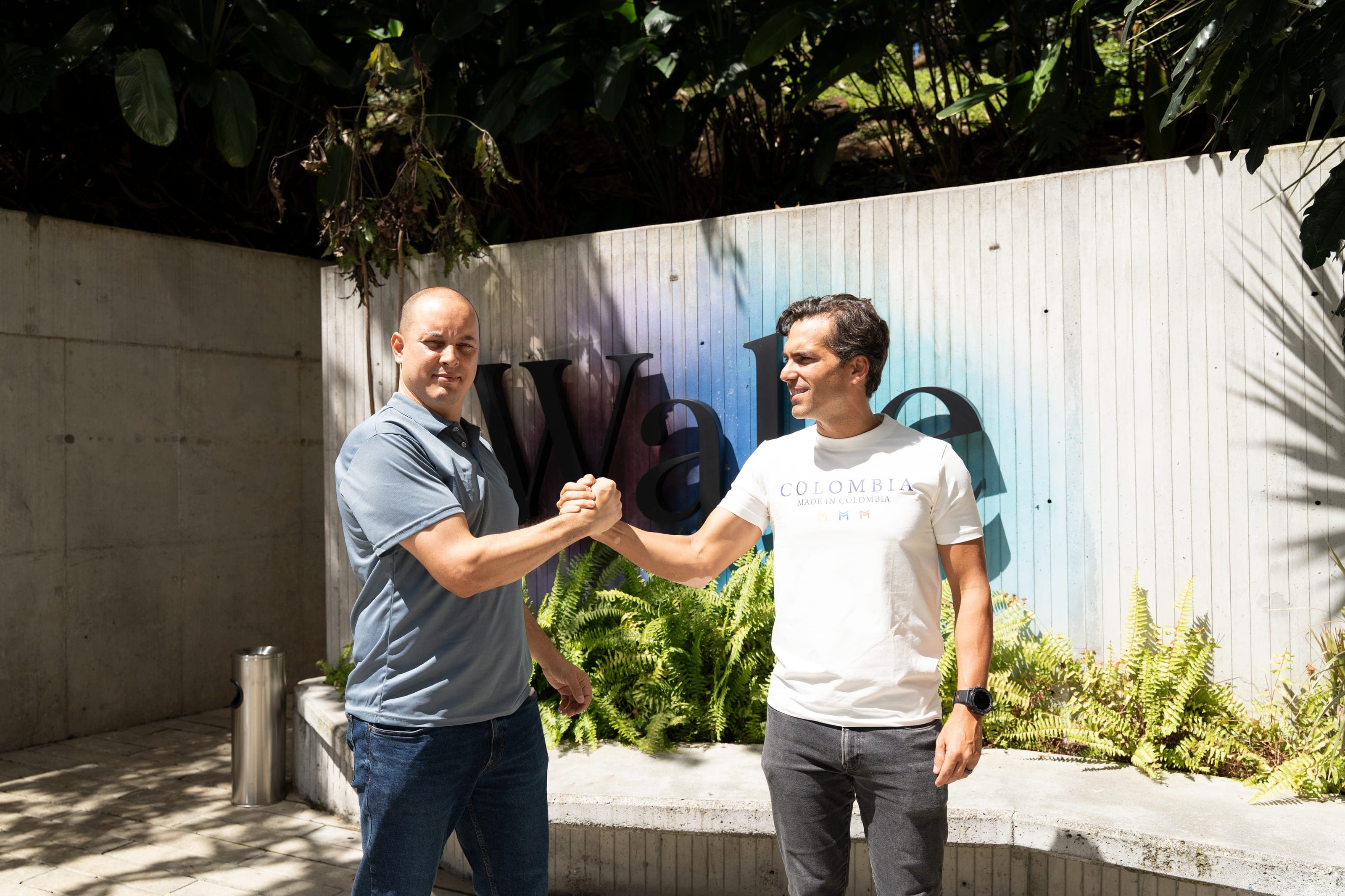 Dos personas se dan la mano frente al muro de Wake, en Medellín, donde Voltop opera una estación de carga